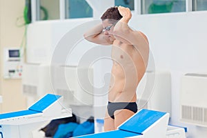 Young muscular swimmer preparing to start, puts his hat and glasses.