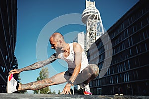 Young muscular tattooed man doing exercises, stretching early in the morning