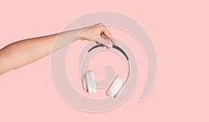 Young music fan showing modern headphones on pink background, close up