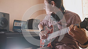 Young musician composes and records soundtrack playing the guitar using computer, headphones and keyboard