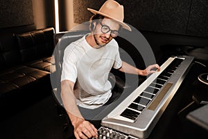 Young musician composing new song on midi piano in sound recording studio. Attractive guy playing on electric piano in