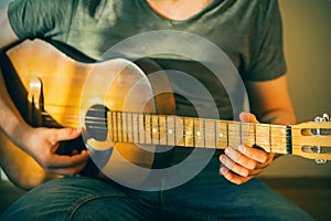 A young musician in a green t-shirt and blue jeans plays an old acoustic guitar