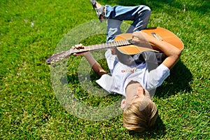 A young musician is lying on the green grass with a guitar in his hands, top view