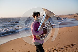 Young musician playing the tuba on the sea coast. Hobby.