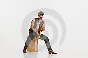 Young musician in retro style outfit playing saxophone isolated over white studio background. Concept of music, hobby