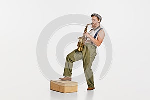 Young musician in retro style outfit playing saxophone isolated over white studio background. Concept of music, hobby