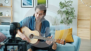 Young musician vlogger recording video for internet music blog playing guitar and talking using camera