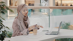 Young muslim businesswoman in hijab sitting in office uses phone stirring coffee in paper cup leisure arab girl reading