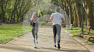 Young muslim couple in sport clothes standing in start position for run at green summer park. Man and woman in hijab