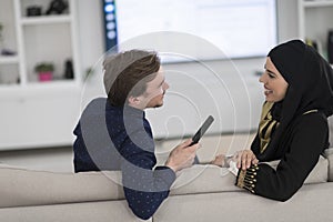 Young muslim couple woman wearing islamic hijab clothes sitting on sofa watching TV together during the month of Ramadan