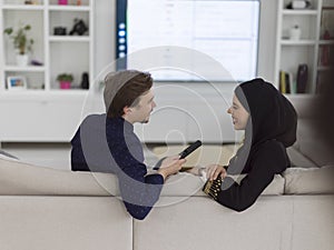 Young muslim couple woman wearing islamic hijab clothes sitting on sofa watching TV together during the month of Ramadan