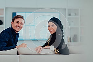 Young muslim couple woman wearing islamic hijab clothes sitting on sofa watching TV together during the month of Ramadan