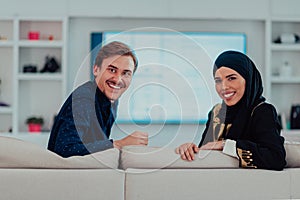 Young muslim couple woman wearing islamic hijab clothes sitting on sofa watching TV together during the month of Ramadan