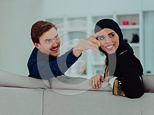 Young muslim couple woman wearing islamic hijab clothes sitting on sofa watching TV together during the month of Ramadan