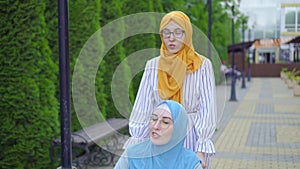 Young muslim disabled in a traditional scarf in a wheelchair communicates with a muslim friend on the street close up