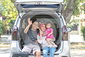 Young muslim family , transport, leisure, road trip and people concept - happy man, woman and little girl sitting on trunk of