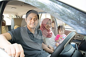 Young muslim family , transport, leisure, road trip and people concept - happy man, woman and little girl traveling in a car looki