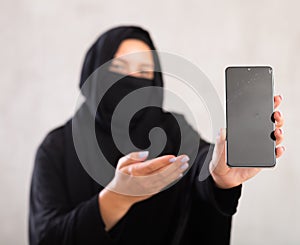 young Muslim girl with her face covered by burka shows empty dark smartphone screen.