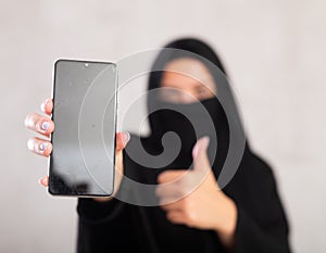 young Muslim girl with her face covered by burka shows empty dark smartphone screen.