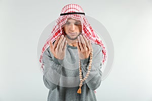 Young Muslim man praying on light background