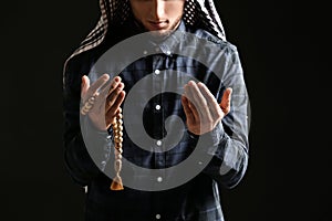 Young Muslim man with rosary beads praying on dark background