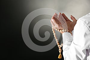 Young Muslim man with rosary beads praying on dark background, closeup