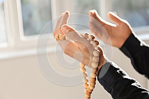 Young Muslim man with rosary beads praying at home, closeup