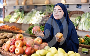 Young Muslim woman in abaya and chador choosing apples in store