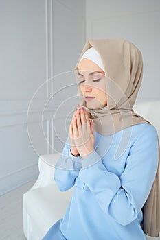 Young muslim woman in beige hijab and traditional clothes praying with eyes closed for Allah, muslim God