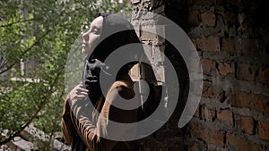 Young muslim woman in black hijab holding her hands and looking upwards, standing in abandoned brick building