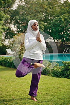 Young muslim woman doing yoga by the poolside