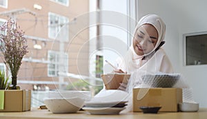 Young muslim woman in hijab confirming orders from customer on mobile phone. Small business owner, Online selling, E-commerce