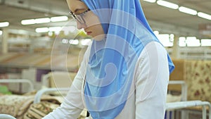 Young muslim woman in a hijab and glasses in a carpet store