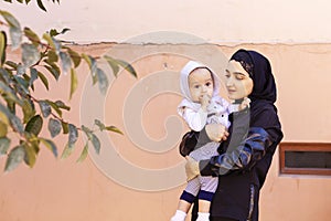 Young Muslim woman in hijab holding her 1-year-old baby boy, hugging and kissing. Happy Muslim mother in abaya clothing kiss and