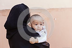 Young Muslim woman in hijab holding her 1-year-old baby boy, hugging and kissing. Happy Muslim mother in abaya clothing kiss and