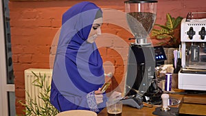 Young muslim woman in hijab making credit card payment, taking coffee and going away, smiling