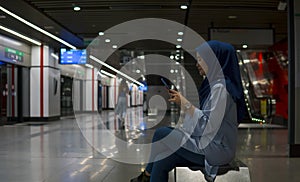 Young Muslim woman inside subway train station sitting while using phone.