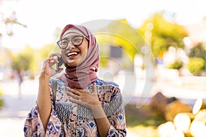 Young muslim woman laughing while using mobile phone