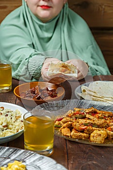 A young Muslim woman in a light khimar at the table takes a flatbread with her hand during Ramadan iftar