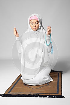 Young Muslim woman praying on light background