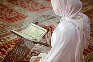 Young muslim woman praying in mosque with quran