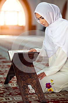 Young muslim woman praying in mosque with quran