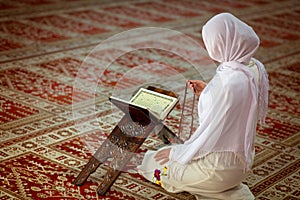 Young muslim woman praying in mosque with quran