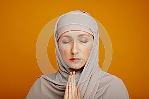 A young muslim woman in the religious concept praying to God with faith and respect. A muslim woman on yellow background