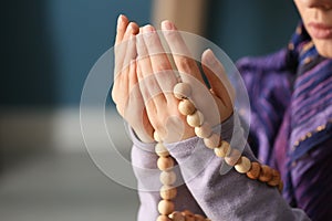 Young Muslim woman with rosary beads praying at home, closeup