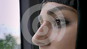 Young muslim woman`s in hijab eyes is watching in rainy window in bus, weather concept, transport concept, urban concept