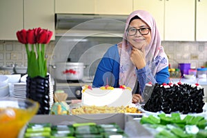 A young muslim woman smiling in a kitchen in front of her cakes that she made. photo