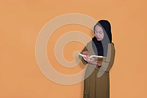 young muslim woman standing and reading the Quran on the yellow background