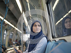 Young Muslim woman traveling inside subway train sitting looking at window.