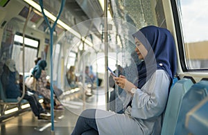 Young Muslim woman traveling inside subway train sitting while using phone.